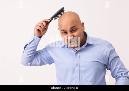 Portrait d'un homme chauve peignant sa tête rasée avec de la frustration sur fond blanc. Banque D'Images