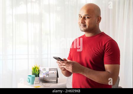 Un homme chauve tenant un téléphone portable dans la main dans une pièce. Banque D'Images
