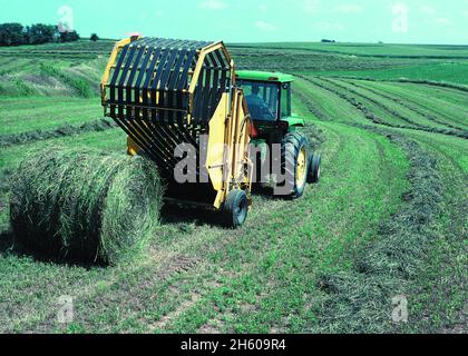 Tracteur John Deere au travail avec une presse à balles rondes.De grosses balles de foin sont produites sur des terres très érodables dans le nord-est de l'Iowa.1999 Banque D'Images