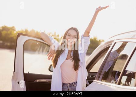 Photo de confiant drôle jeune femme porter chemise blanche lever les bras ouvert porte de voiture sourire à l'extérieur de la rue de ville Banque D'Images