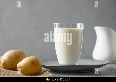 Lait de pomme de terre vegan en verre et pomme de terre dans un bol sur fond gris.Gros plan.Produit de remplacement du lait à base de plantes et sans lactose. Banque D'Images