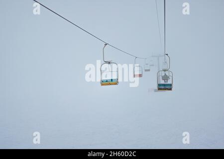 Des téléphériques sont accrochés aux câbles dans une station de ski silencieuse contre un ciel brumeux Banque D'Images