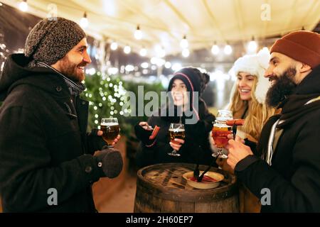 Heureux souriant amis avec des verres à bière s'amuser, passer du temps ensemble à la foire d'hiver le soir.Vacances, concept de Noël Banque D'Images