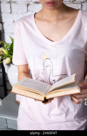 Une fille dans un T-shirt rose tient un livre ouvert dans ses mains Banque D'Images