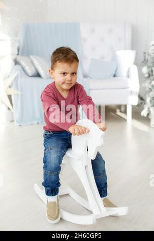 Petit garçon en robe rouge balançant sur un cheval en bois.Le concept d'une enfance heureuse Banque D'Images