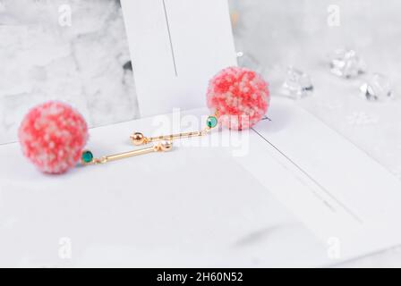 Boucles d'oreilles ornées de bijoux verts avec boules de fourrure roses sur elles.les boucles d'oreilles sont flanquées de cubes de glace transparents et d'autres décorations Banque D'Images