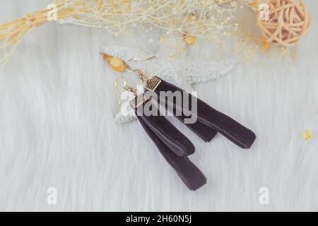 Boucles d'oreilles en forme de banderole noires.À côté des boucles d'oreilles sont des produits en rotin, avec des spécimens de bouquet jaune et d'autres objets décoratifs. Banque D'Images