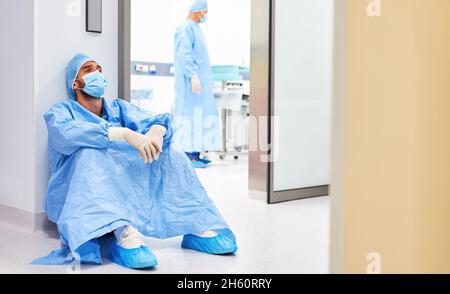 Le chirurgien épuisé est assis sur le sol devant la salle d'opération après une opération fatigante dans la clinique Banque D'Images