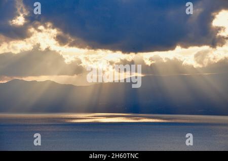 Rayons du soleil qui se déversent dans la mer à travers les nuages.Rayons crépusculaires.Le soleil brille à l'heure d'or jusqu'à la mer.Coucher de soleil orange, partiellement nuageux et coloré avec Banque D'Images