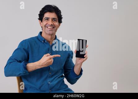 Indien affichant son smartphone assis sur une chaise Banque D'Images