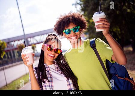 Photo portrait couple souriant portant des lunettes boire des milk-shakes portant des vêtements décontractés marchant dans la ville Banque D'Images