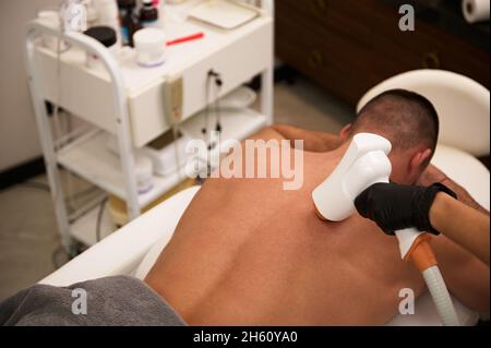 Vue en hauteur d'un jeune sportif allongé sur une table de massage dans le salon de beauté, qui reçoit un traitement au laser au dos.Concept d'épilation masculin.Manly Banque D'Images