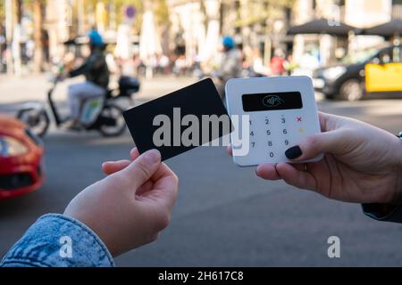 Client méconnaissable avec carte de crédit sans contact payant au vendeur féminin avec terminal sur fond flou de rue de la ville en journée Banque D'Images