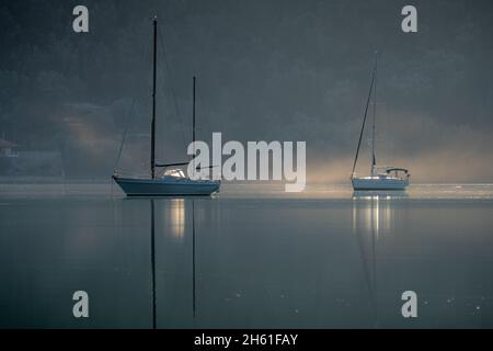 Yachts sur l'eau calme d'une baie abritée en fonte réflexions avec brume matinale sur la surface de l'eau. Banque D'Images