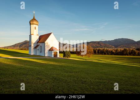 La chapelle baroque de Saint Johann au-dessus de la vallée de Loisach et les préAlpes bavaroises automnales avec le mont Benediktenwand au soleil de soirée, en Allemagne Banque D'Images