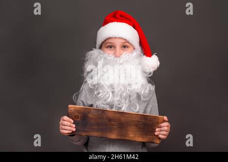 Un garçon de 8-10 ans dans un chapeau et avec une barbe de père Noël. Maquette Banque D'Images