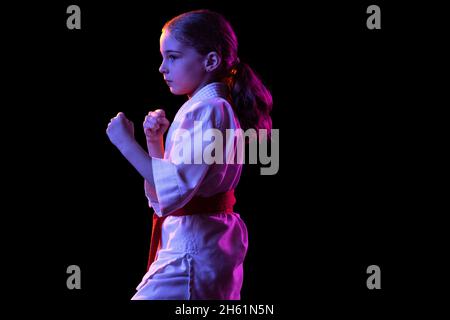 Une petite fille, jeune karaté en position de combat isolée sur fond sombre.Concept du sport, de l'éducation, des compétences Banque D'Images