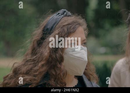 Une petite fille en gros plan se promenant dans le parc avec un masque de visage à l'extérieur pendant une excursion.Voyager pendant le concept de virus corona. Banque D'Images