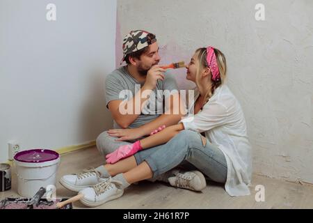 Une jeune famille heureuse fait une réparation de rêve à l'intérieur de la maison avec ses propres mains.Mari et femme peignent le mur de la chambre Banque D'Images