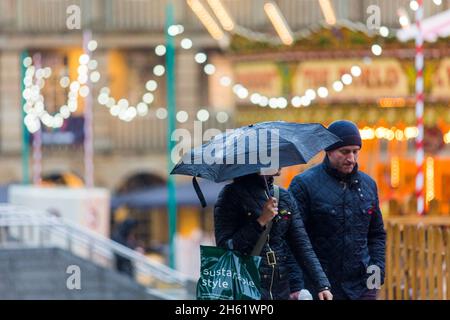 Un couple porte un parapluie comme ils font leurs achats de Noël dans le Halifax Piece Hall , Calvaire , West Yorkshire.Le mauvais temps et la forte pluie ne les ont pas stoppe. Banque D'Images