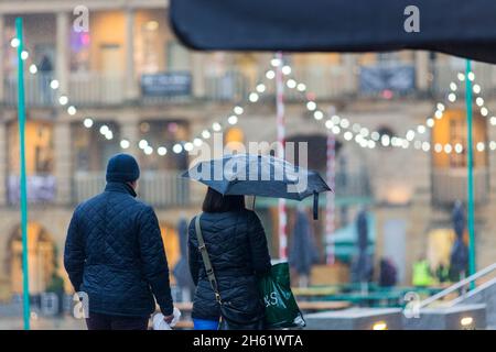 Un couple brave la pluie dans le Halifax Piece Hall, à Calvaire, dans le West Yorkshire, pour faire ses courses de Noël dans le bâtiment historique . Banque D'Images