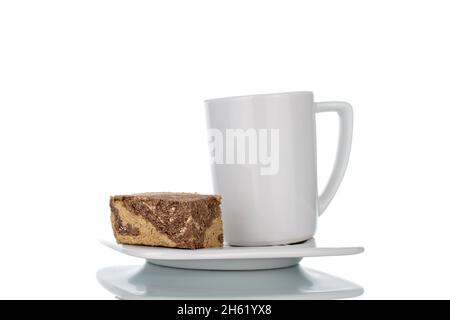 Morceaux de halva douce au chocolat sur une soucoupe blanche avec une tasse blanche, gros plan, isolé sur blanc. Banque D'Images