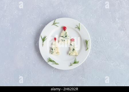 arbres du nouvel an fabriqués au fromage roquefort et décorés de raisins de corinthe rouges, sur une assiette, fond gris, vue de dessus Banque D'Images