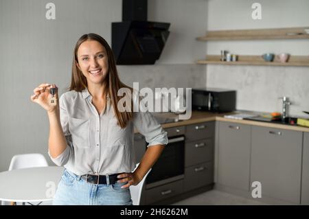 Bonne jeune femme tenant les clés avec porte-clés sous forme de petite maison.Une dame brune souriante tient les clés de la nouvelle propriété, heureux acheteur de sa propre propriété, relocalisée Banque D'Images