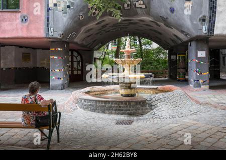 une femme est assise sur un banc à la hundertwasserhaus près de la fontaine, löwengasse angle kegelgasse, 3ème arrondissement, landstrasse, vienne, autriche Banque D'Images