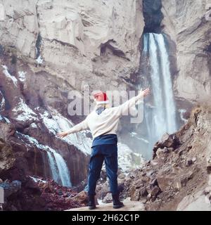 Femme dans un chapeau de Père Noël, tire ses mains vers les cascades.Concept festif.Grande cascade Banque D'Images