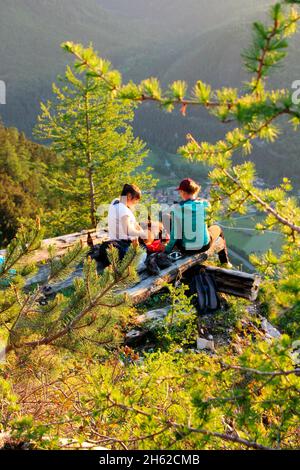 deux jeunes femmes,snack,sont heureux dans le contre-jour,coucher de soleil,photographié à la cabane mittenwalder à la karwendel,mittenwald,haute-bavière,vallée d'isar,bavière,allemagne,europe,larches,branches de mélèze Banque D'Images