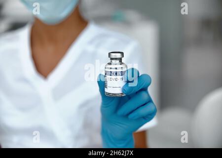 Vaccin contre le coronavirus en flacon de verre dans la main du médecin.Bocal de vaccin sur fond blanc dans un glovs bleu.Vaccin concept de lutte contre le coronavirus Banque D'Images