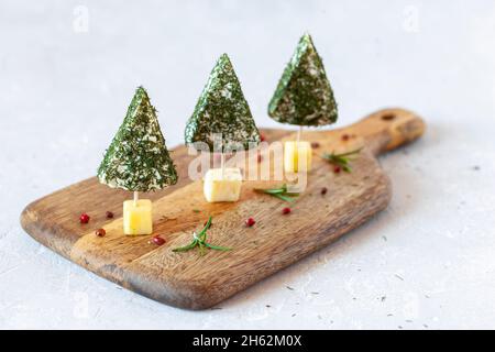 Hors-d'œuvre d'arbres de Noël en fromage doux sur une planche à découper sur fond blanc, gros plan, vue latérale Banque D'Images