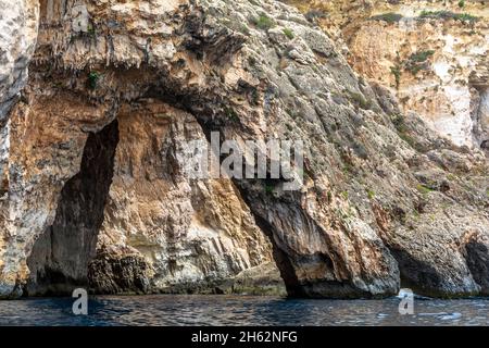 Les bords rocailleux de la Grotte bleue, Malte, s'en sortant de la mer Méditerranée et éclairé par le soleil du matin.Formations rocheuses avec grottes. Banque D'Images