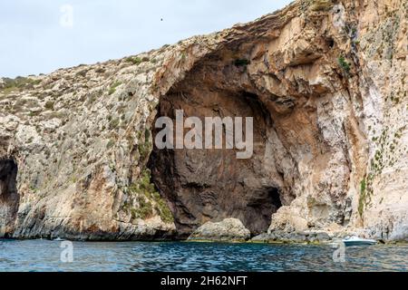 Les bords rocailleux de la Grotte bleue, Malte, s'en sortant de la mer Méditerranée et éclairé par le soleil du matin.Formations rocheuses avec grottes. Banque D'Images