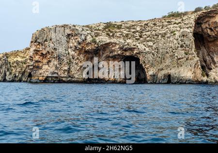 Les bords rocailleux de la Grotte bleue, Malte, s'en sortant de la mer Méditerranée et éclairé par le soleil du matin.Formations rocheuses avec grottes. Banque D'Images