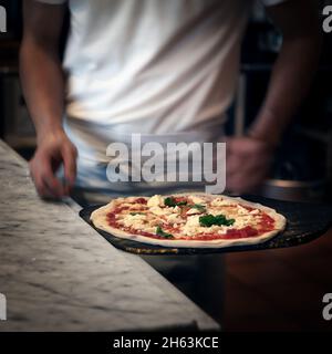 Un chef met la touche finale à une pizza margherita en route vers le four dans une pizzeria de Kamakura, au Japon. Banque D'Images