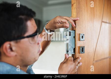 Vue rapprochée des mains mâles, réparation ou installation d'une serrure de porte en métal. Banque D'Images