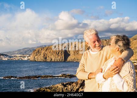 portrait de deux personnes âgées et matures appréciant l'été sur la plage en regardant la mer souriant et en s'amusant avec le coucher du soleil à l'arrière-plan. deux personnes âgées actives voyageant à l'extérieur. Banque D'Images