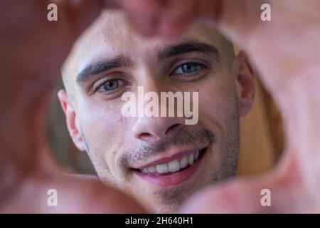 un adolescent affectueux et joyeux prend un portrait romantique de selfie en regardant l'appareil photo à travers le coeur des doigts joints. un jeune garçon épris montrant son amour à l'appareil photo faisant une forme de coeur avec ses mains Banque D'Images