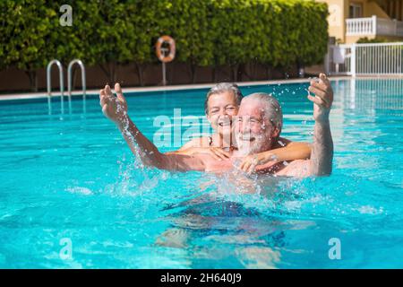 couple de deux aînés heureux s'amuser et s'amuser ensemble dans la piscine souriant et jouant. les gens heureux appréciant l'été dehors dans l'eau Banque D'Images