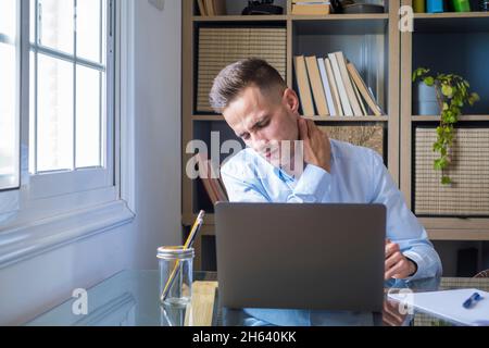 nerfs pincés, muscles endoloris tendus, douleur fibromyalgie due à un mode de vie sédentaire et à une mauvaise posture concept. origine ethnique caucasienne frowning homme assis à un bureau devant un ordinateur portable, toucher le cou ressent de la douleur Banque D'Images