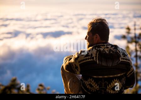 un homme voyage et explorer des lieux pittoresques concept - activités de randonnée en plein air avec des hommes assis sur la falaise et profiter du coucher du soleil et de la vue sur les nuages - détente et la liberté de vie Banque D'Images