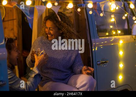 les femmes d'âge moyen aiment la vie nocturne assis à l'extérieur dans une camionnette classique et boire du vin avec des ampoules jaunes - les femmes heureux célébrant ensemble en amitié riant beaucoup Banque D'Images