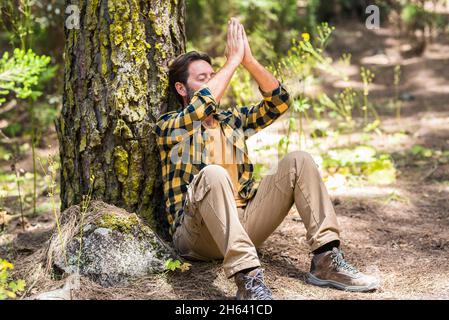 homme adulte dans la forêt assis sur le terrain faisant la méditation et se sentir amoureux des bois dehors nature autour - concept de mode de vie sain et heureux des gens paisibles Banque D'Images