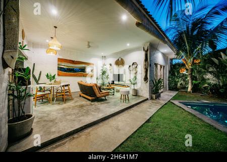 Vue sur la villa tropicale avec jardin, piscine et salon ouvert au coucher du soleil Banque D'Images