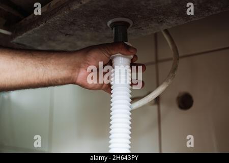 Plombier installe un tuyau de siphon sur l'évier de cuisine.Rénovation dans l'appartement.Élimination des fuites dans l'évier. Banque D'Images