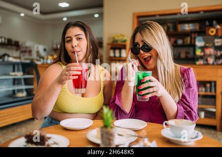 Jeunes filles latines plus grandes assis dans un café écoutant l'histoire de la vie drôle de leur ami Banque D'Images