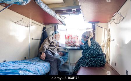 Un homme et une femme kazakh âgés assis dans la voiture de classe 3, regardant par la fenêtre dans un chariot de chariots à plateau dans le train exploité par le Kazakhstan Temir Zholy Banque D'Images