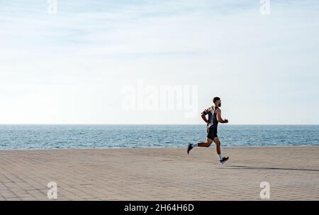Mettre en forme un jeune homme qui court le long du front de mer.Un coureur de sexe masculin fait du jogging tôt le matin.Athlète en train de faire de l'entraînement physique à l'extérieur.Entraînement pendant l'outsi de maintien Banque D'Images